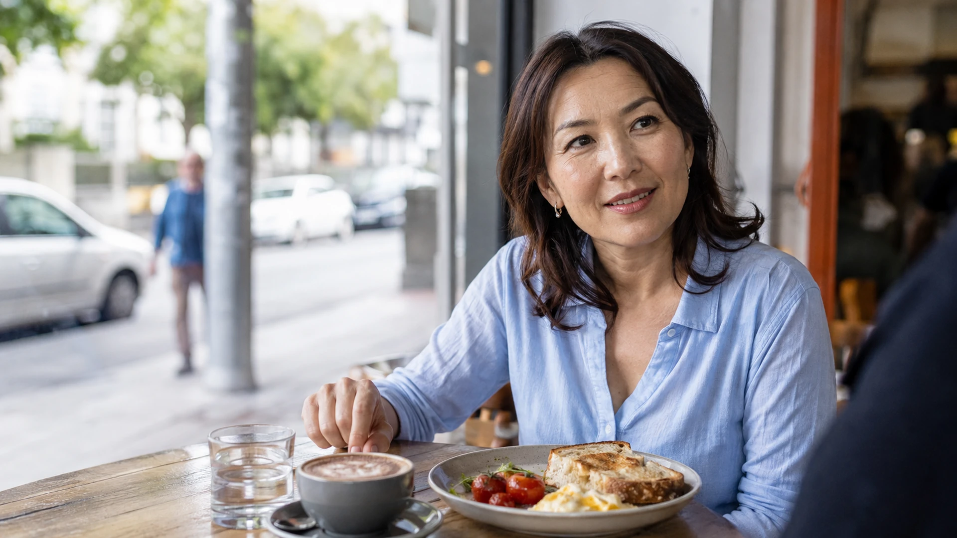 Woman enjoying a relaxed weekend brunch beside a cafe window.